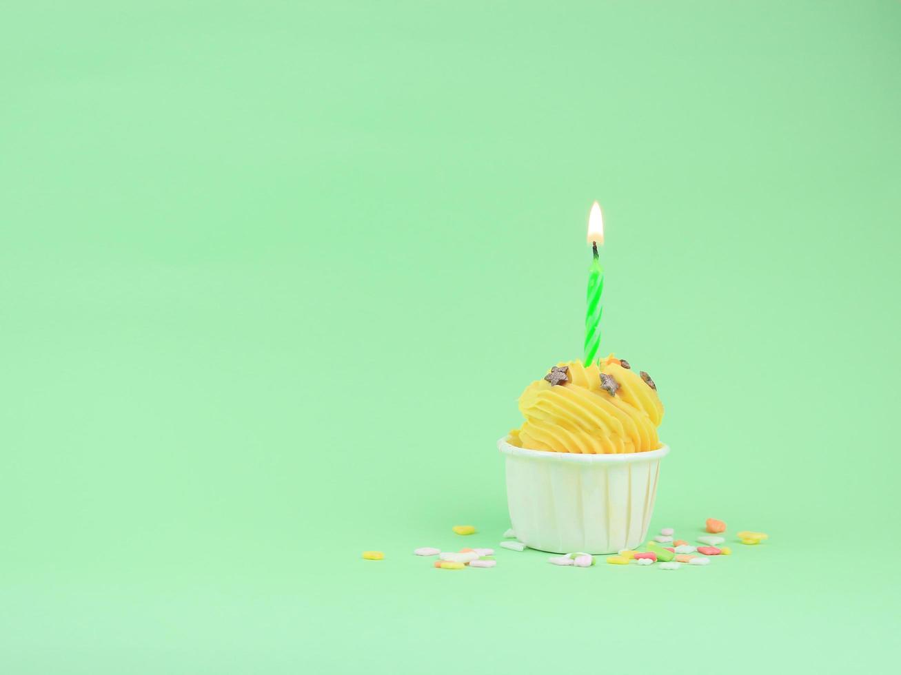 dulce cupcake amarillo con vela de arco sobre fondo verde con espacio para copiar. concepto de fondo de fiesta de feliz cumpleaños. foto