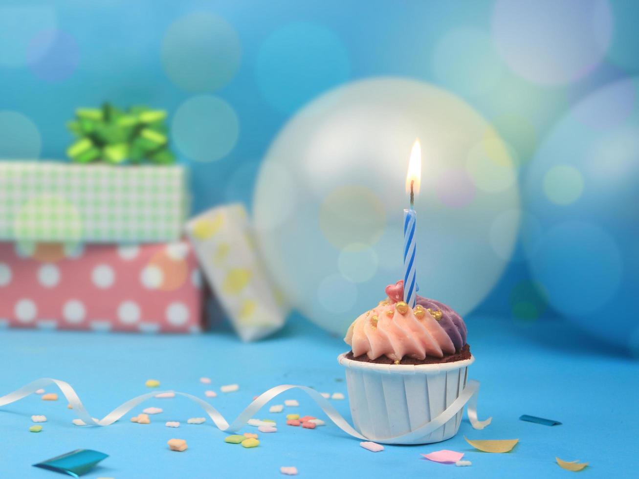 Sweet cupcake and bow candle on blue background with copy space. Happy birthday party photo