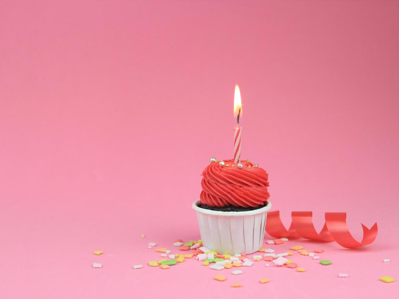 Sweet red cupcake with bow candle on pink background with copy space. Happy birthday party background concept. photo