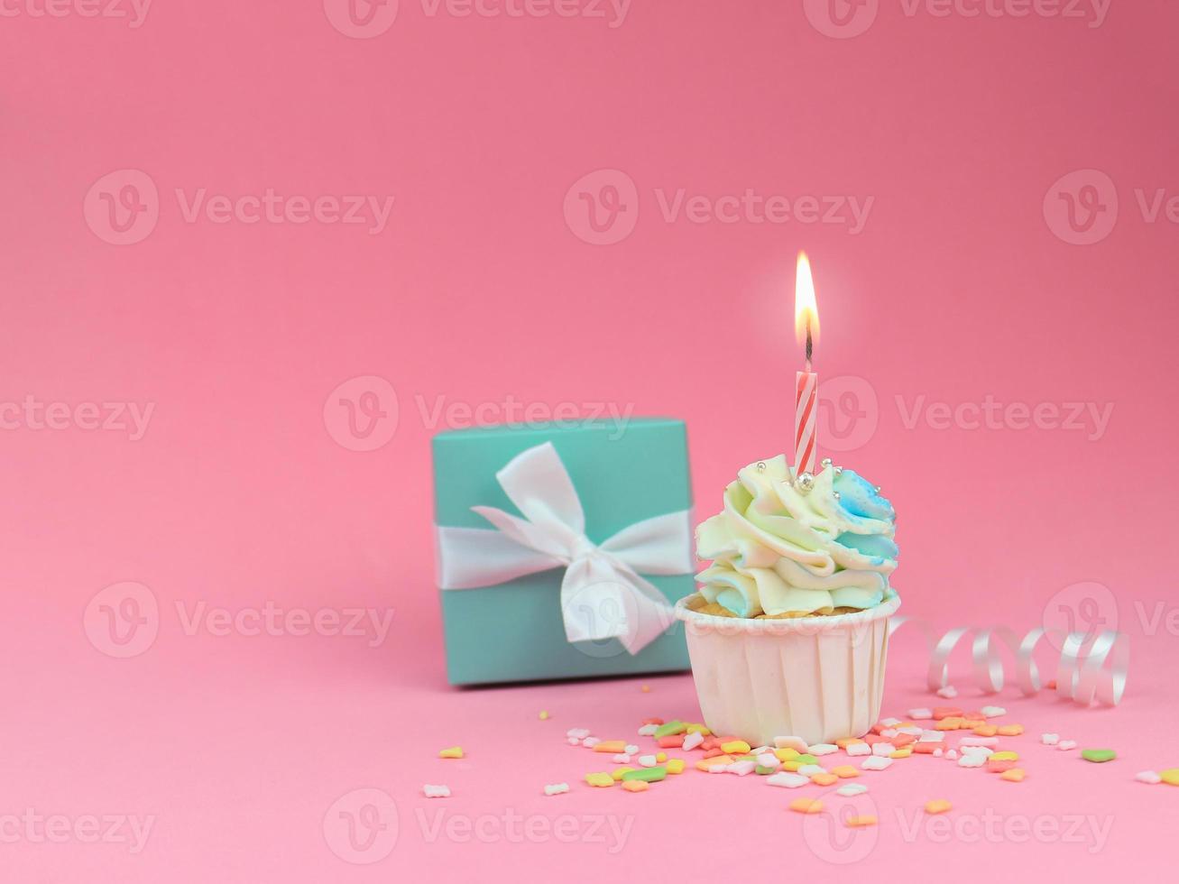 Sweet cupcake with bow candle and gift box on pink background with copy space. Happy birthday party background concept. photo