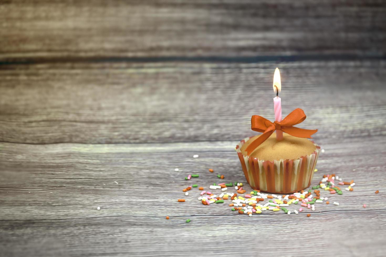 Happy birthday cupcake and bow candle on table on wooden background with copy space. Cute food happy birthday background concept photo