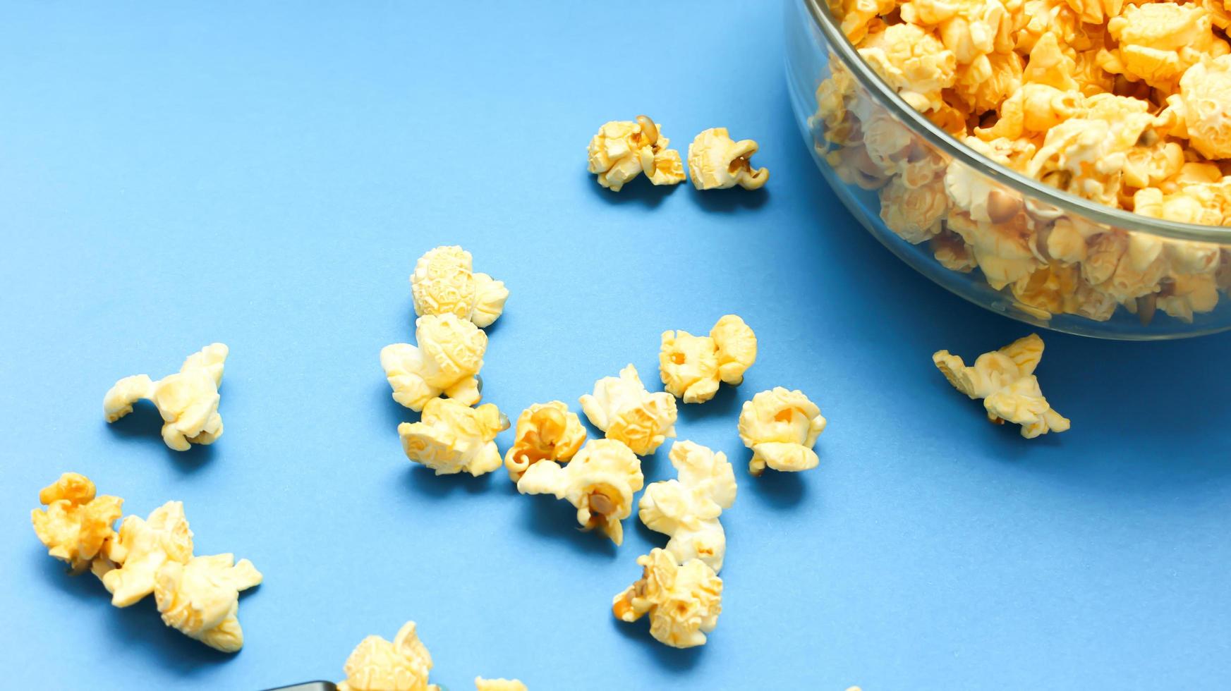 Delicious caramel popcorns sweet dessert on blue background, snacks in a glass bowl for favorite movie times. photo