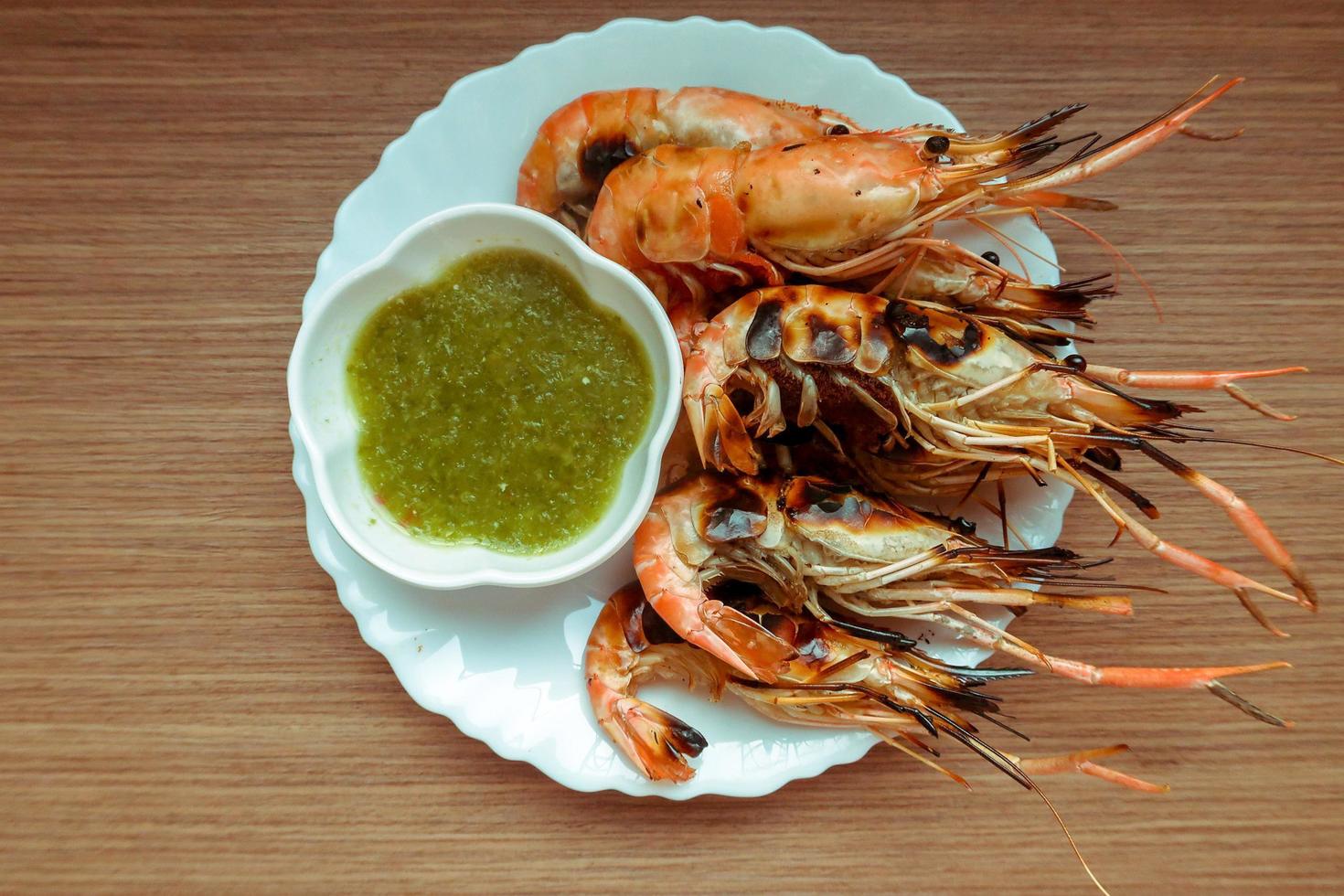 Burned river shrimp, grilled shrimp with spicy green chili seafood sauce in white plate on wooden table photo