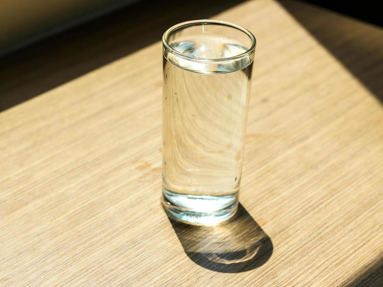 agua potable limpia en el vaso sobre una mesa de madera con el sol brillando a través de la ventana. foto