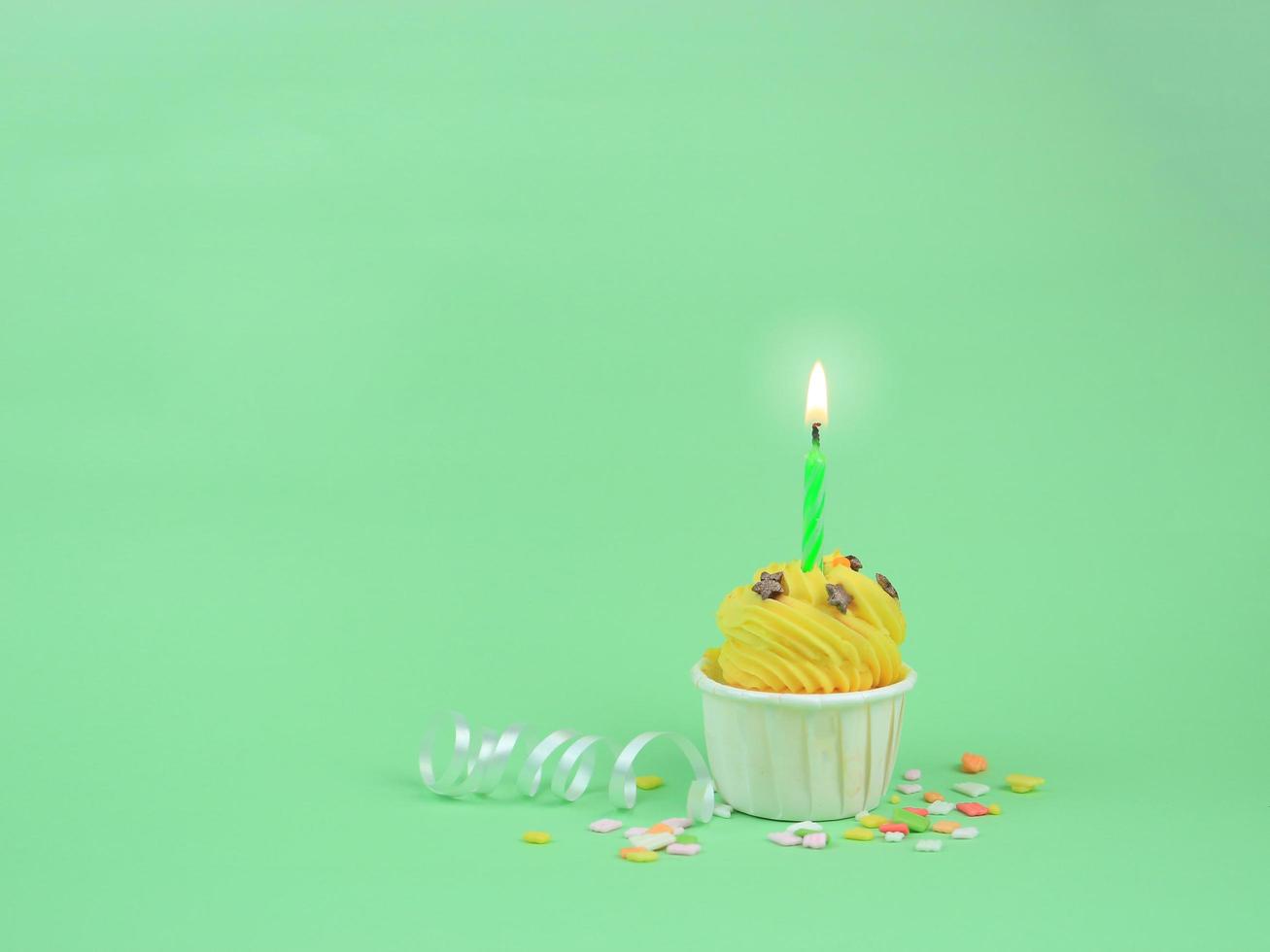 Sweet yellow cupcake with bow candle on green background with copy space. Happy birthday party background concept. photo