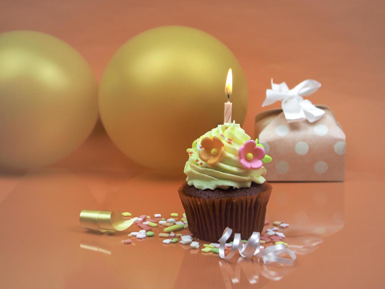 Sweet cupcake with bow candle, gift box present and balloon on orange background. Happy birthday party concept. photo