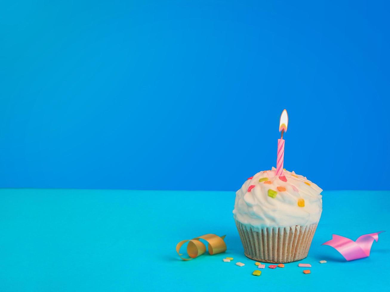 Happy birthday cupcake and bow candle on blue background with copy space. photo