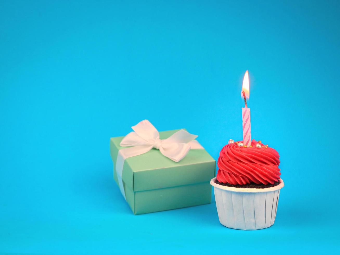 pastelito rojo dulce con vela de arco y caja de regalo sobre fondo azul con espacio para copiar. Fondo de concepto de fiesta de feliz cumpleaños. foto