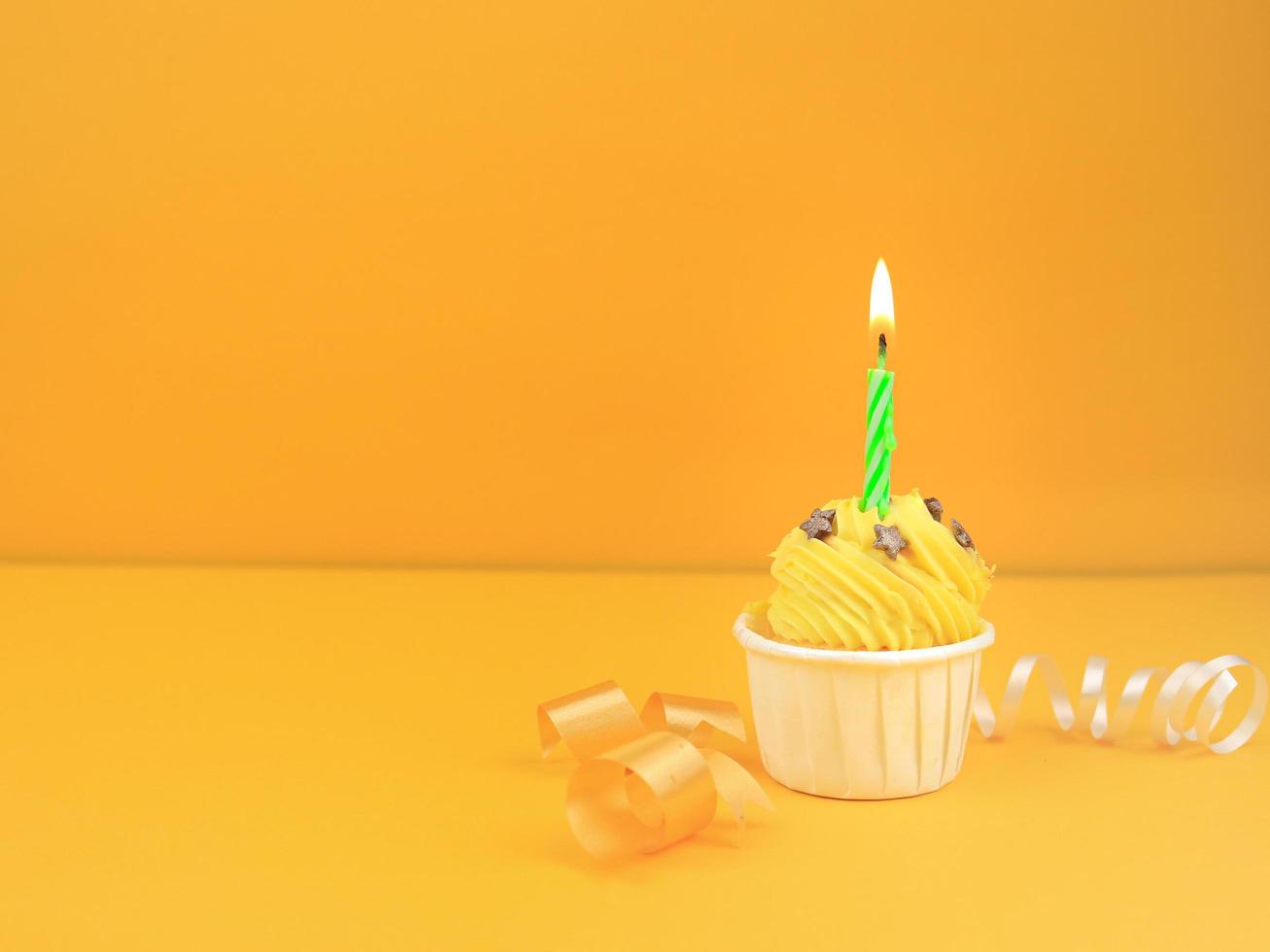 Sweet cupcake with bow candle on yellow background with copy space. Happy birthday party concept background. photo