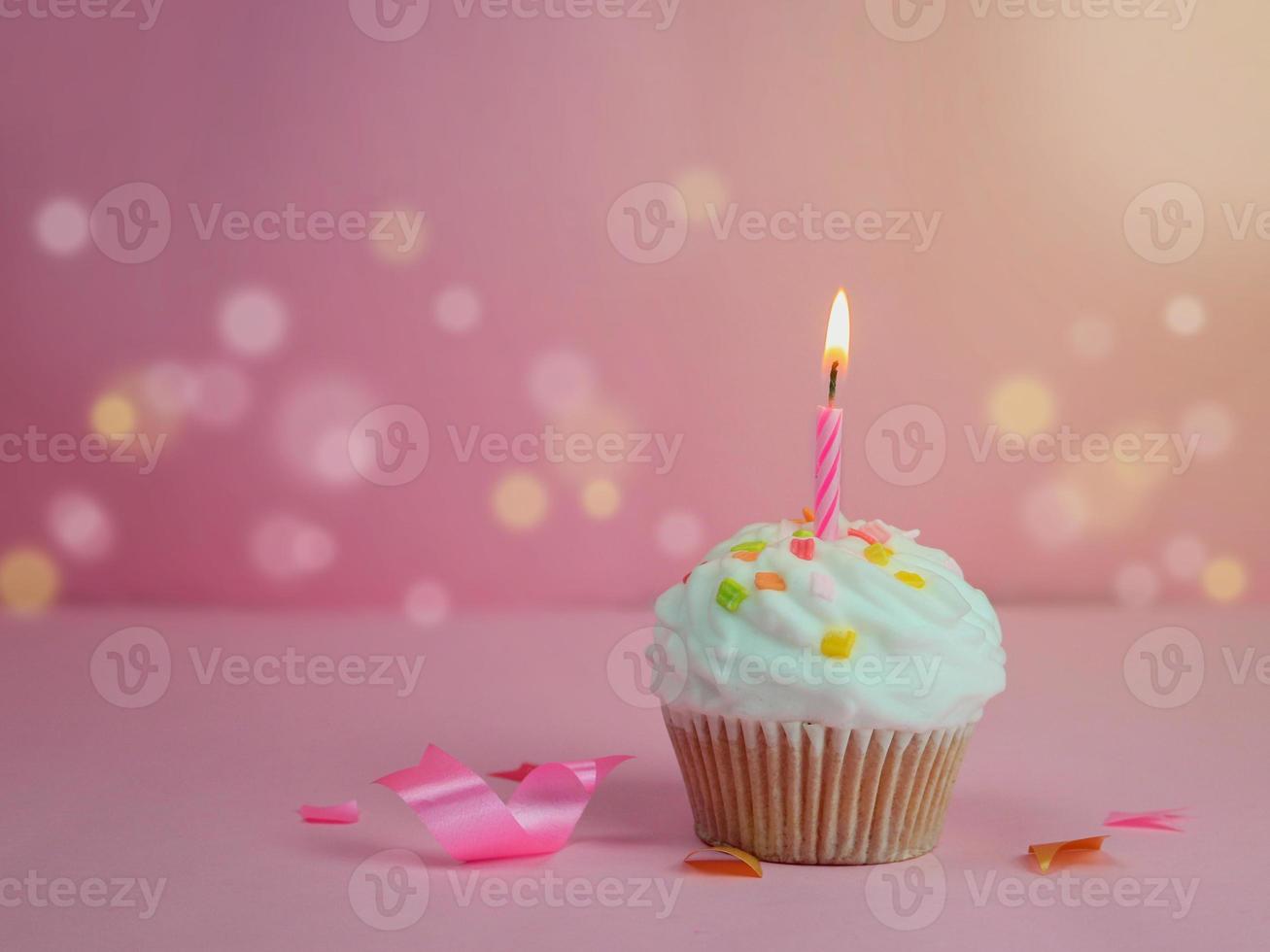 cupcake de feliz cumpleaños y vela de arco sobre fondo rosa con espacio de copia. foto