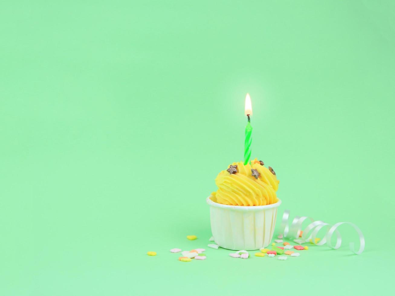 Sweet yellow cupcake with bow candle on green background with copy space. Happy birthday party background concept. photo