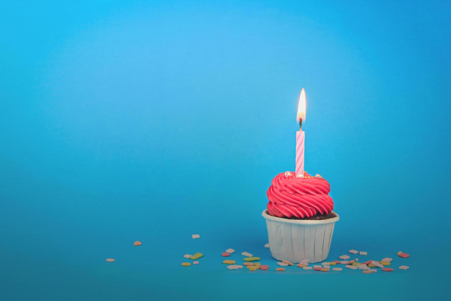 pastelito rojo dulce con vela de arco sobre fondo azul con espacio de copia. Fondo de concepto de fiesta de feliz cumpleaños. foto