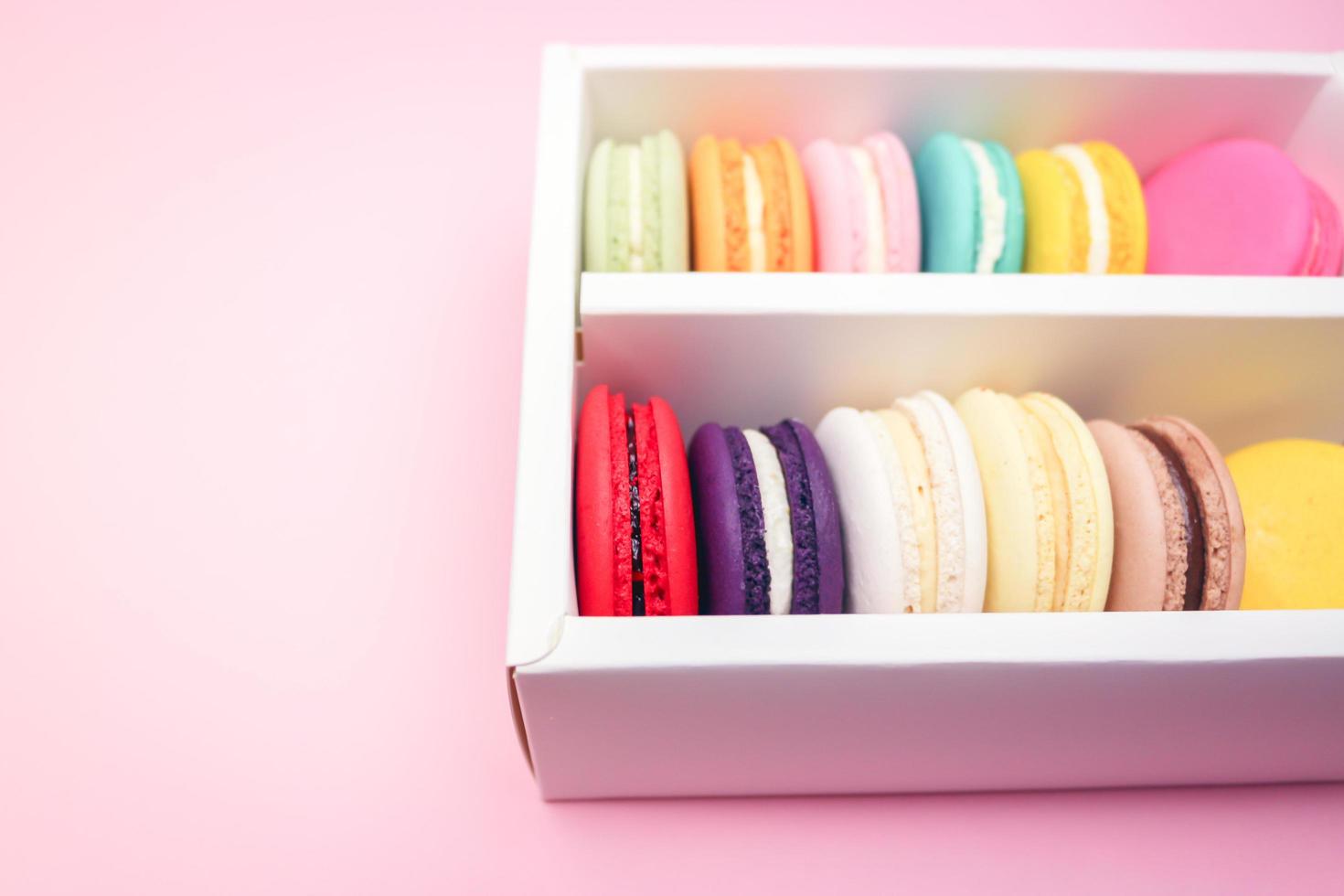 Colorful french macarons macaroons cake in carton box, delicious sweet dessert on a pink background with copyspace, food background concept. photo