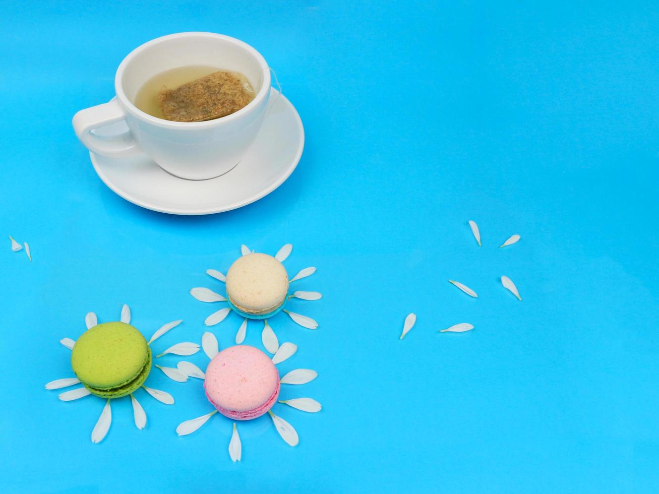 A cup of tea with cute colorful French macarons macaroons , delicious sweet dessert on blue background, lovely food background concept. photo