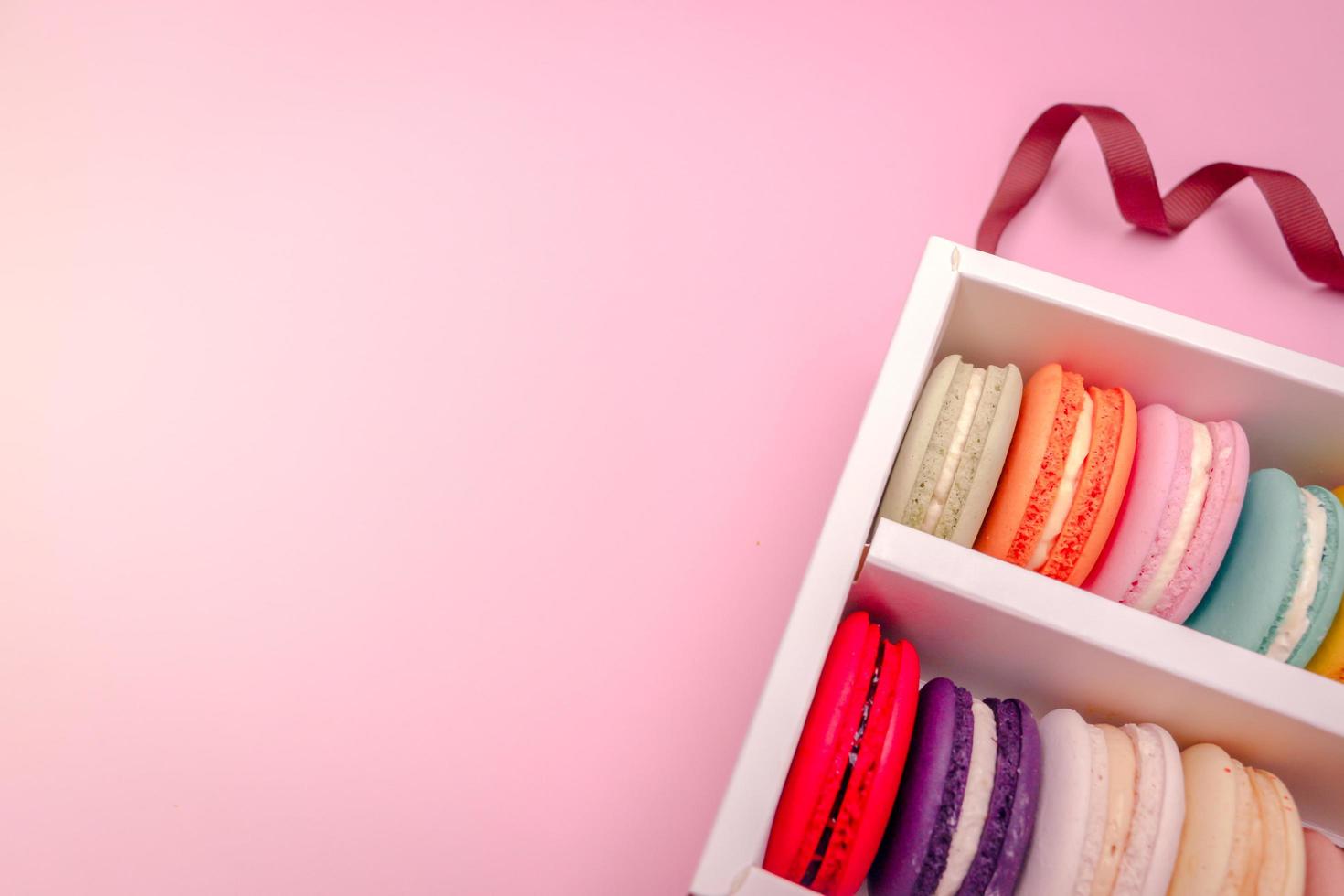 Colorful french macarons macaroons cake in carton box, delicious sweet dessert on a pink background with copyspace, food background concept. photo