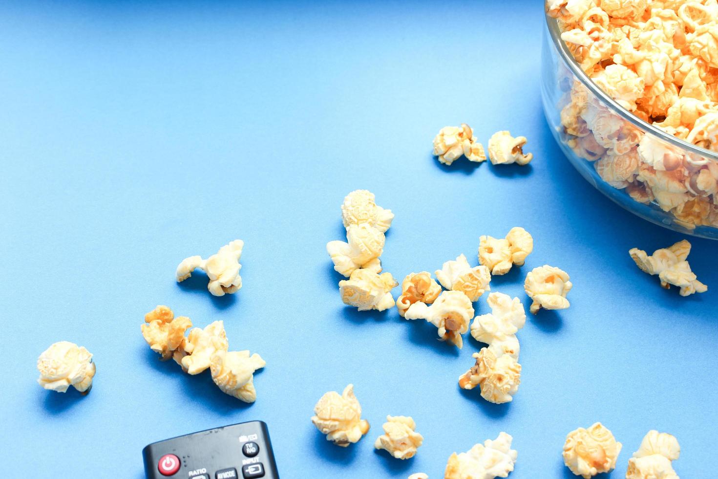 delicioso postre dulce de palomitas de caramelo sobre fondo azul, bocadillos en un tazón de vidrio para los momentos favoritos de cine. foto
