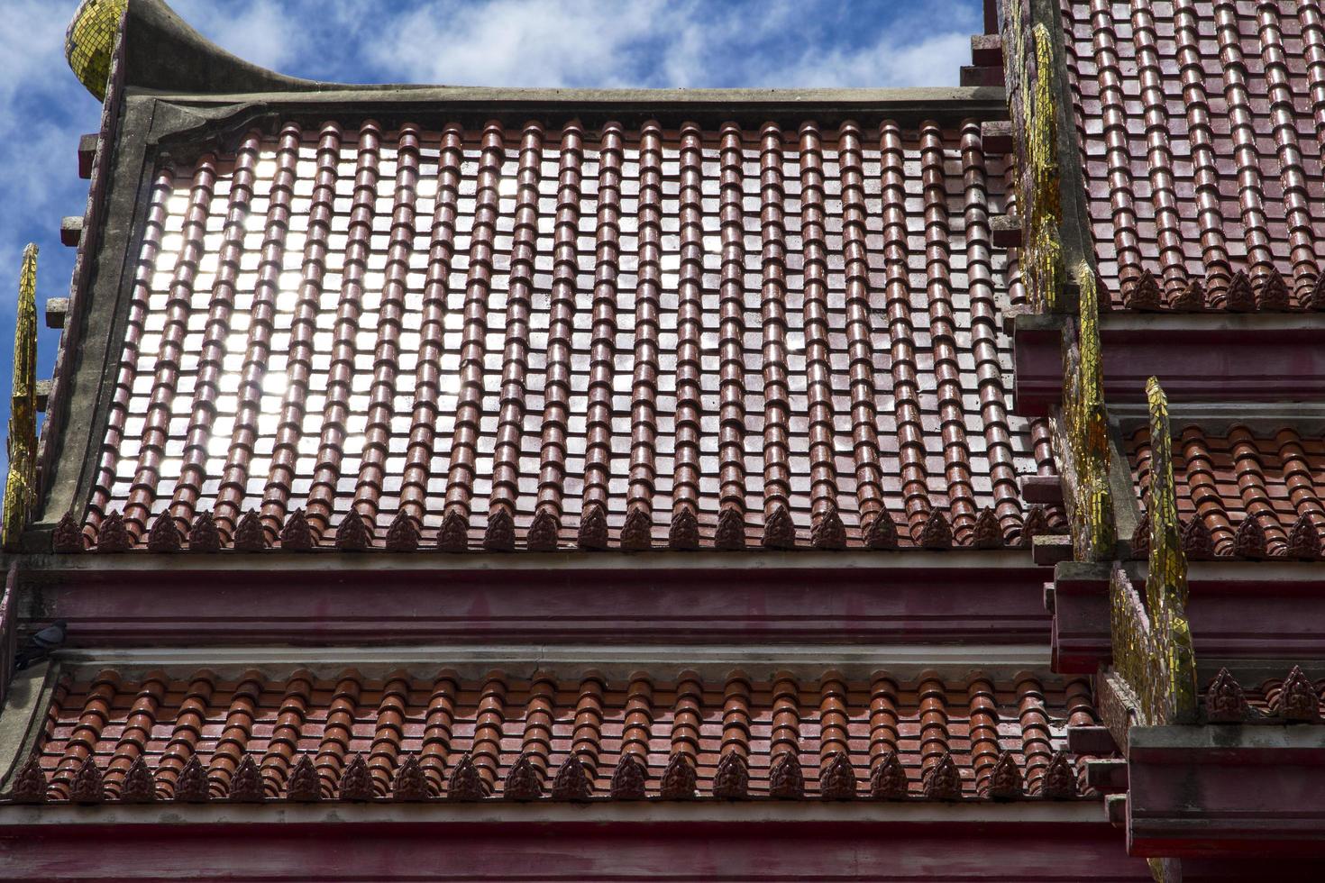 Red roof of a Thai temple with-gable apex- is a delicate Thai art created by skilled craftsmen. And in all Thai temples it is the same art in the blue sky on a sunny day. photo