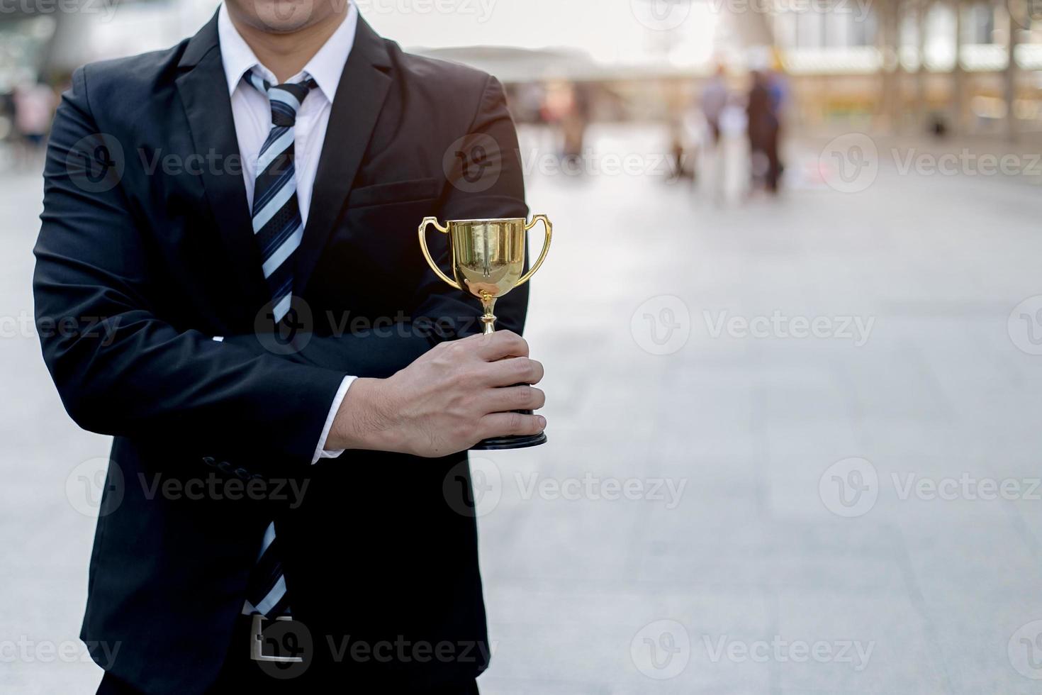 businessman, holding up a gold trophy cup is winner in a competition with city background. Win concept. photo