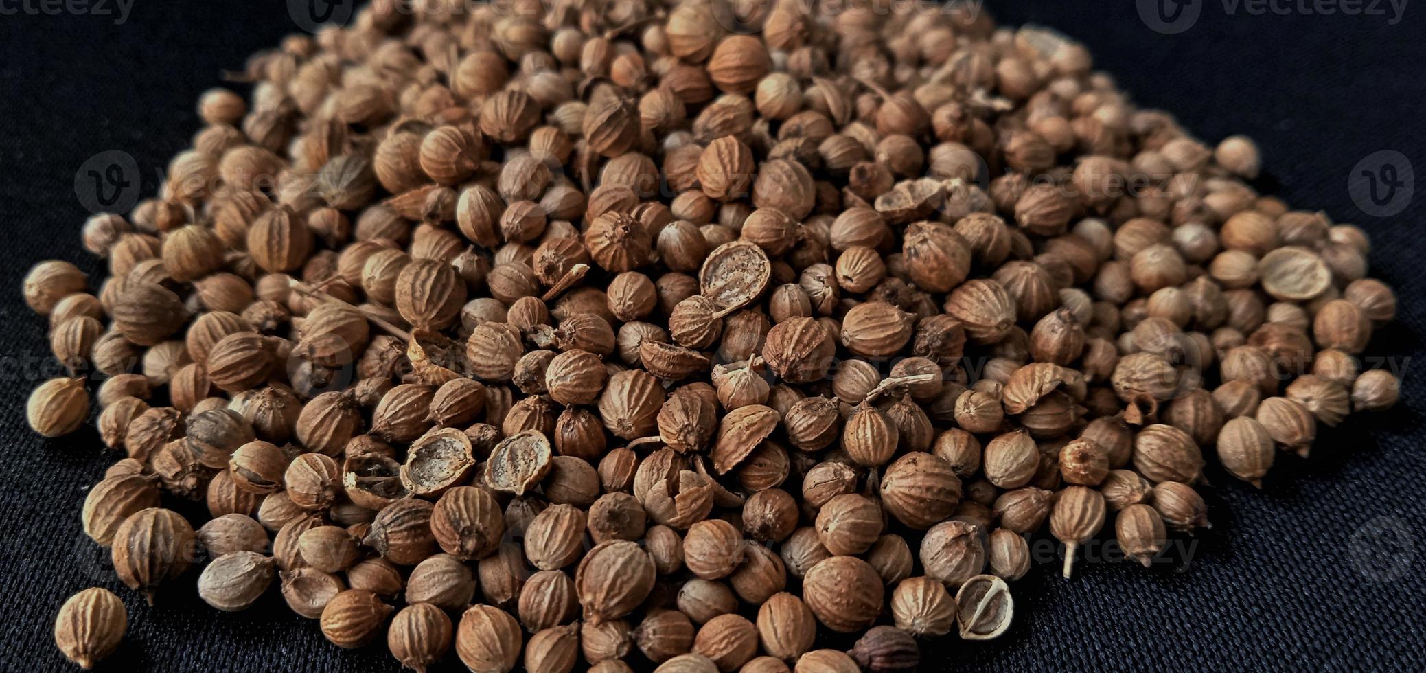 A spreaded dried coriander seed on black background. Ingredient background design. Available for text. Suitable for the food advertising of company and industry, poster, backdrop, flyer, etc. photo