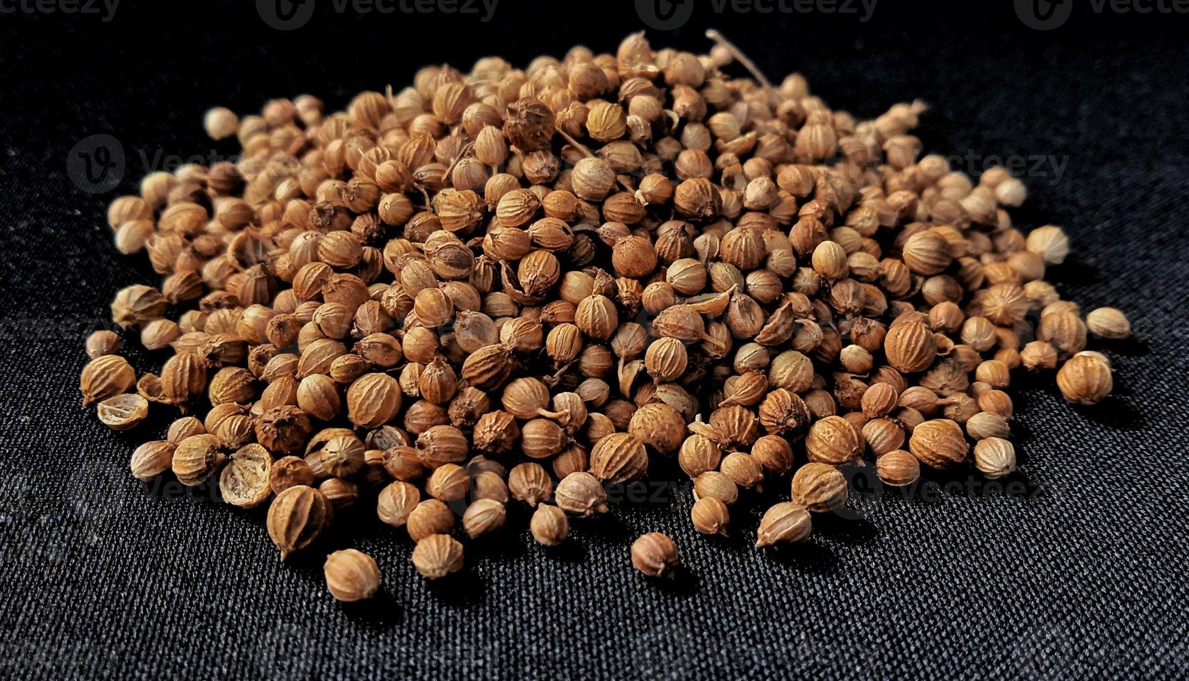 A spreaded dried coriander seed on black background. Ingredient background design. Available for text. Suitable for the food advertising of company and industry, poster, backdrop, flyer, etc. photo