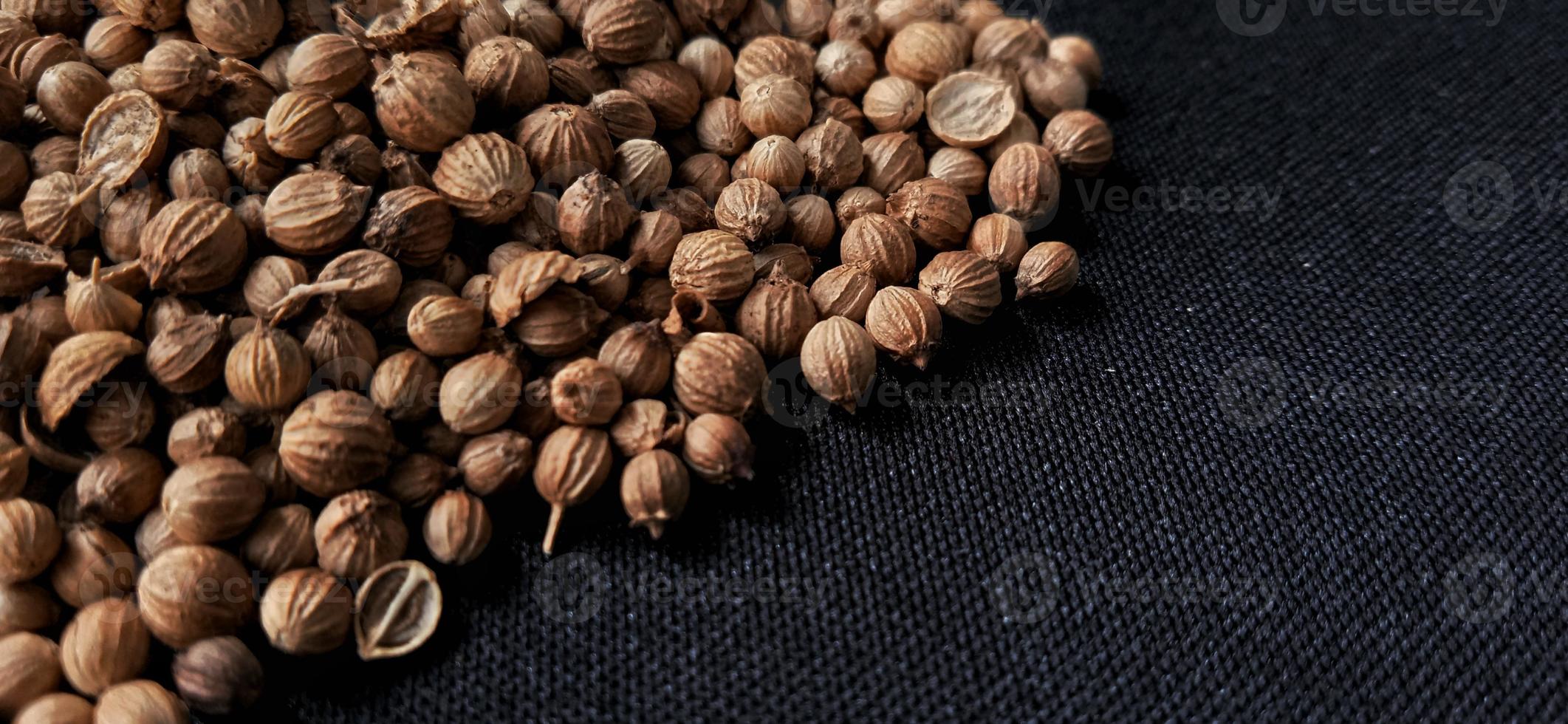 A spreaded dried coriander seed on black background. Ingredient background design. Available for text. Suitable for the food advertising of company and industry, poster, backdrop, flyer, etc. photo