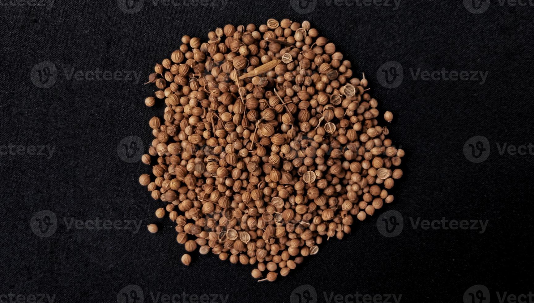 A spreaded dried coriander seed on black background. Ingredient background design. Available for text. Suitable for the food advertising of company and industry, poster, backdrop, flyer, etc. photo