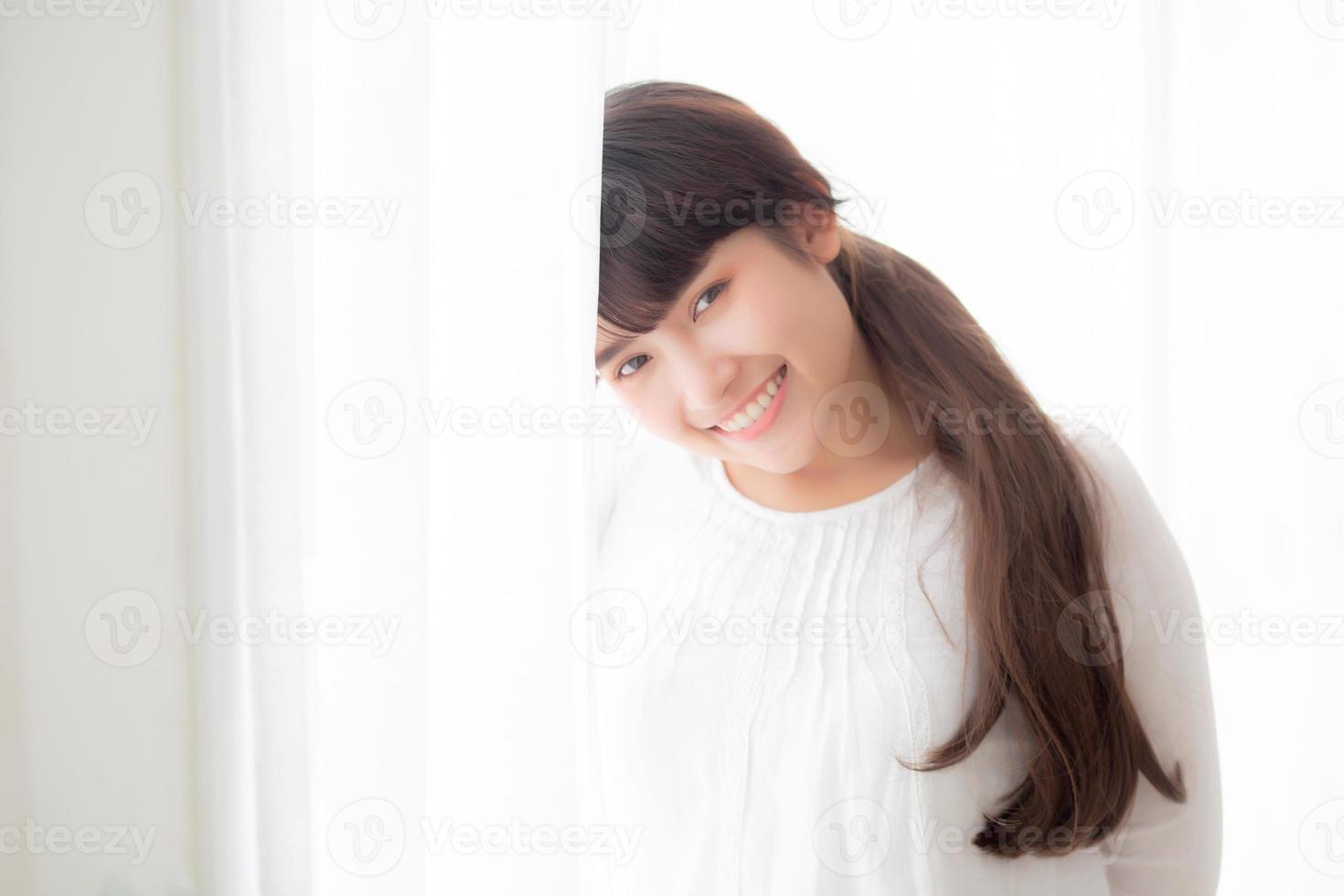 Portrait of beautiful young asian woman standing the window and smile while wake up with sunrise at morning, girl happy with freshness and cheerful, lifestyle and relax concept. photo