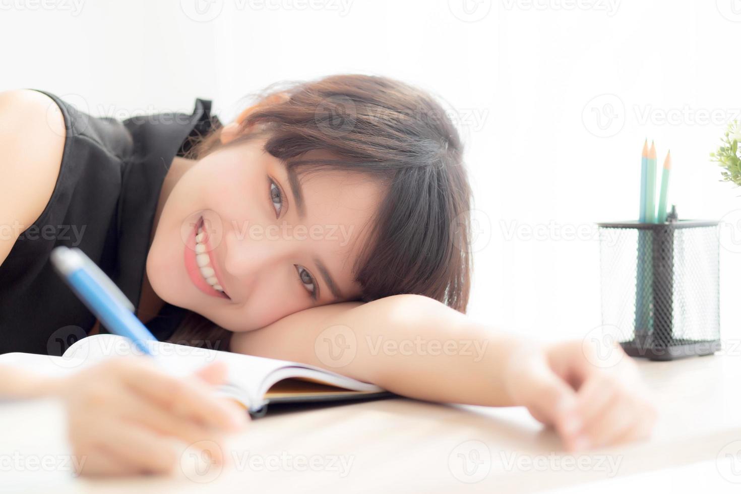 hermoso retrato joven mujer asiática sonrisa y feliz escritura aprendizaje examen o tarea y acostado con escritorio, estilo de vida belleza asia chica con trabajo, educación y concepto de negocios. foto