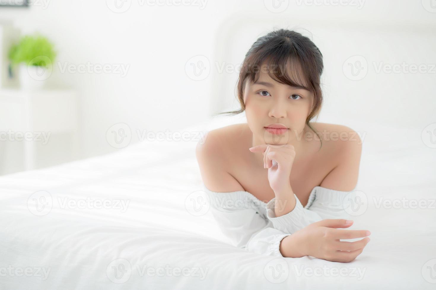 hermoso retrato joven mujer asiática acostada y sonriendo mientras se despierta con el amanecer en la mañana, belleza linda chica feliz y alegre descansando en la cama en el dormitorio, estilo de vida y concepto de relajación. foto