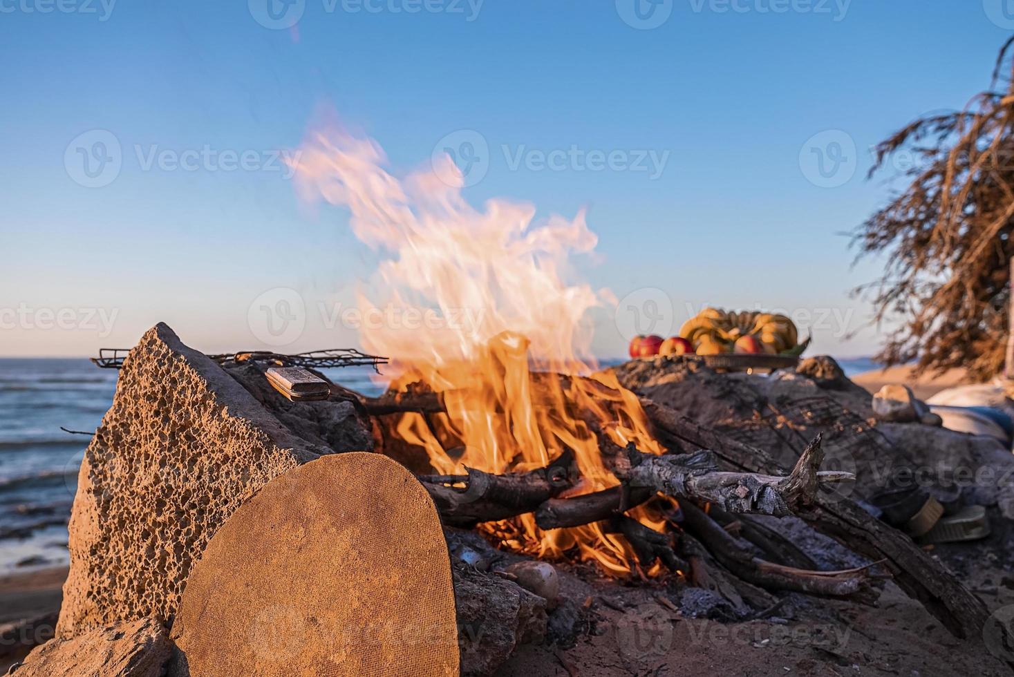 Bonfire with burning firewood on beach in evening against clear sky photo