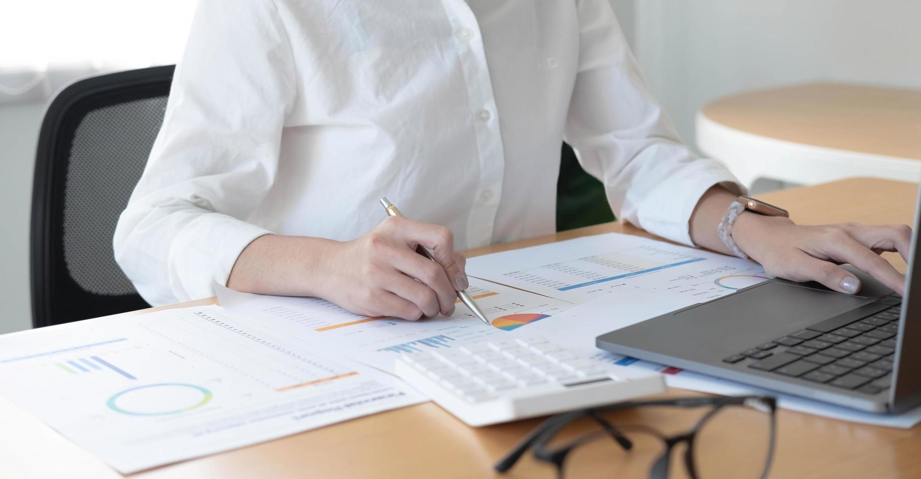 Businesswoman working at office with calculator and laptop computer calculating financial report graph data documents on desk, close up, business analysis, work process concept photo