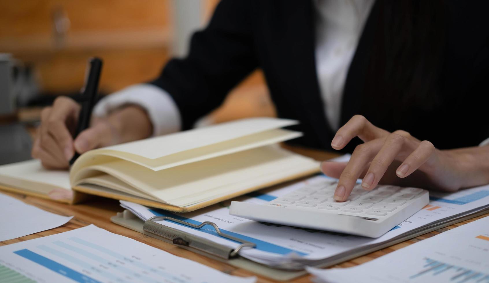 mano de mujer de negocios que sostiene la calculadora de uso de pluma y el punto del dedo en el gráfico de estadísticas de crecimiento y el gráfico en el papeleo para el análisis y cálculo de la contabilidad financiera del presupuesto. foto