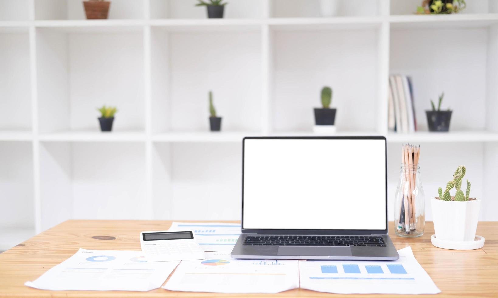 Close up of modern office desktop with blank white notebook screen, smartphone, coffee cup, supplies and other items. Mock up photo