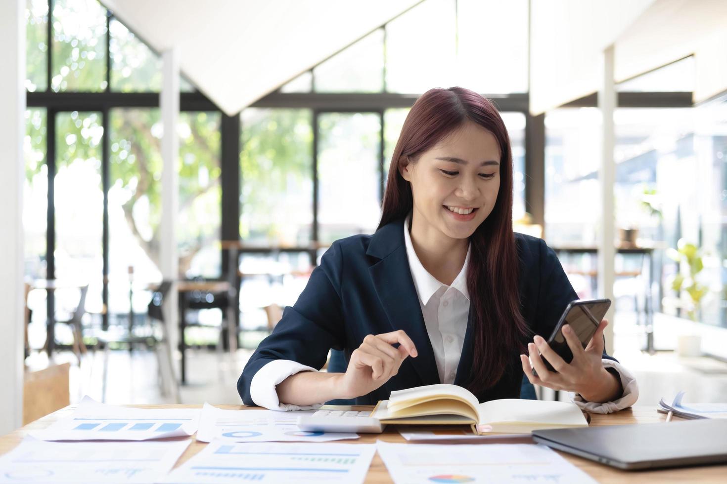 Asian woman talking on the phone and working on a laptop with a smiling face, Business Cell Phone Conversations, Working at cafe, cafe lifestyle, Stay cafe, New normal, learning, Social distancing. photo