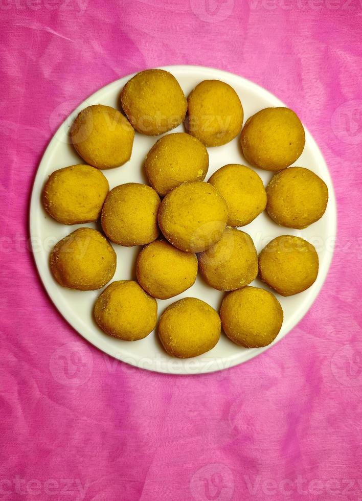 festival indio dulce - besan laddu, hecho con harina de gramo, azúcar y ghee, colocado en un plato blanco sobre un fondo de color. foto