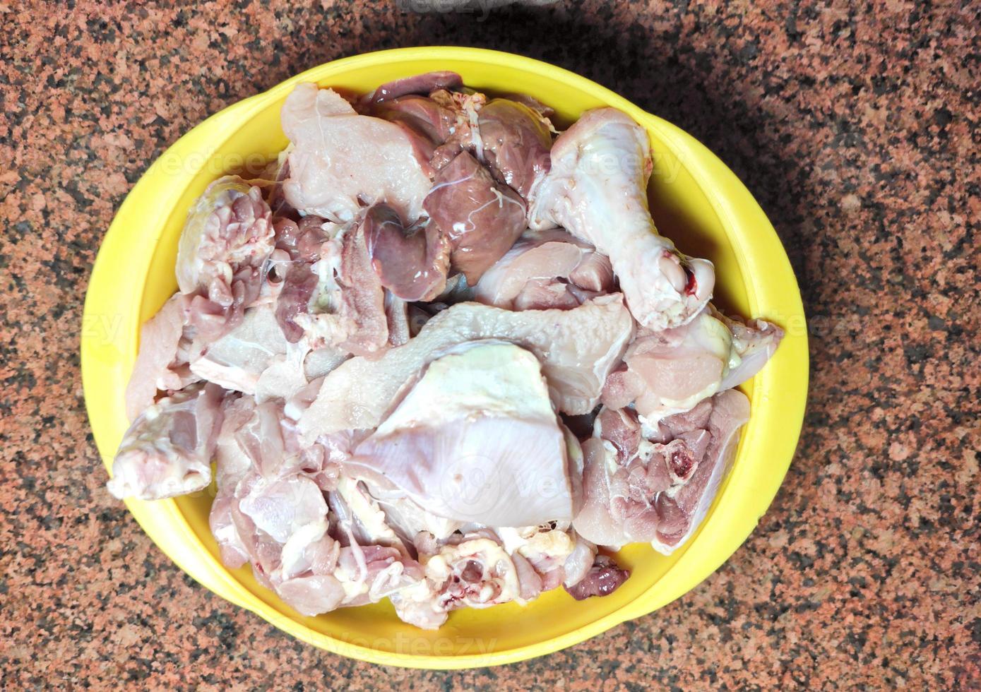 Raw chicken pieces in yellow bowl on brown background photo