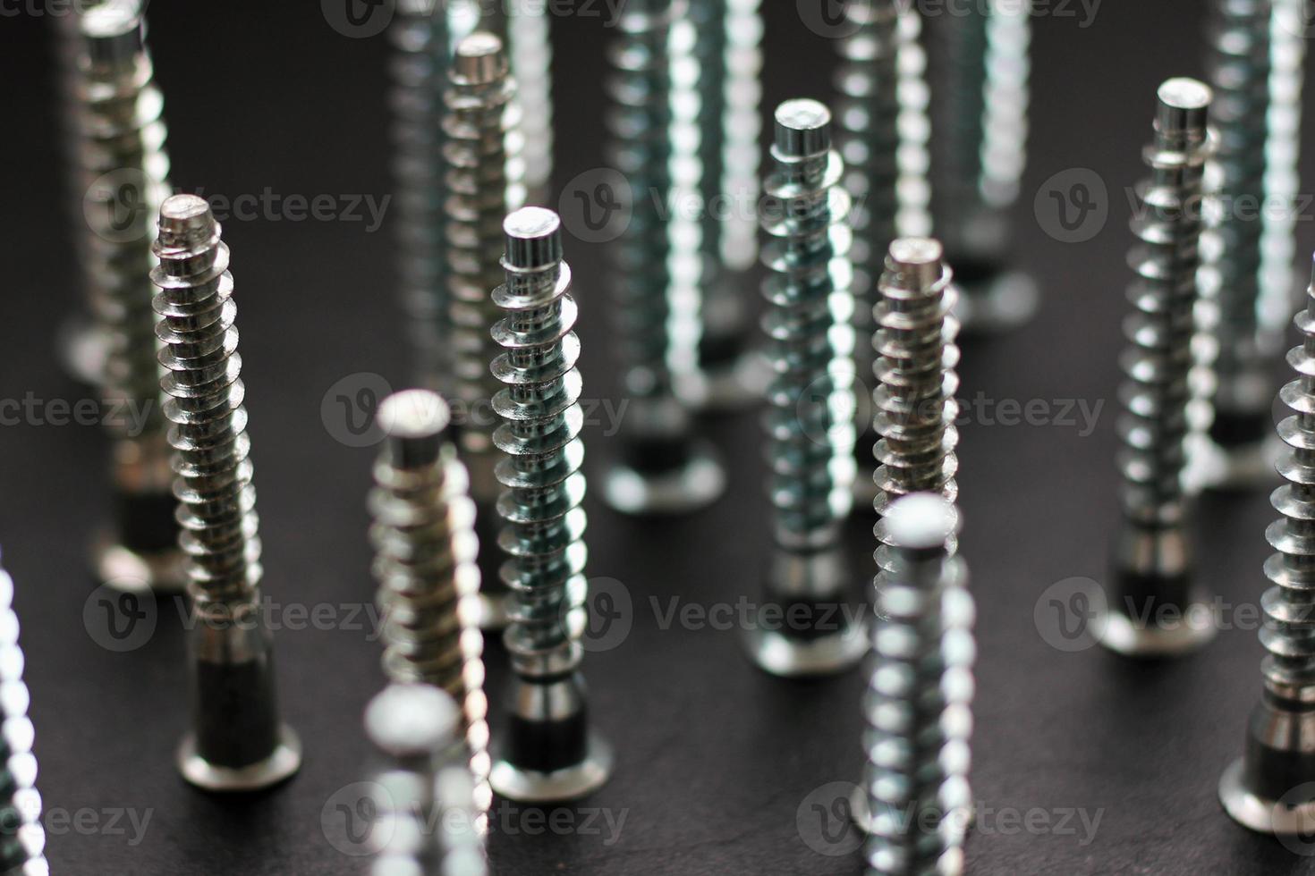 Standing vertically screws tool on black blurred background, selective focus, horizontal photo. Group of iron or metal screws for repair and construction, closeup photo