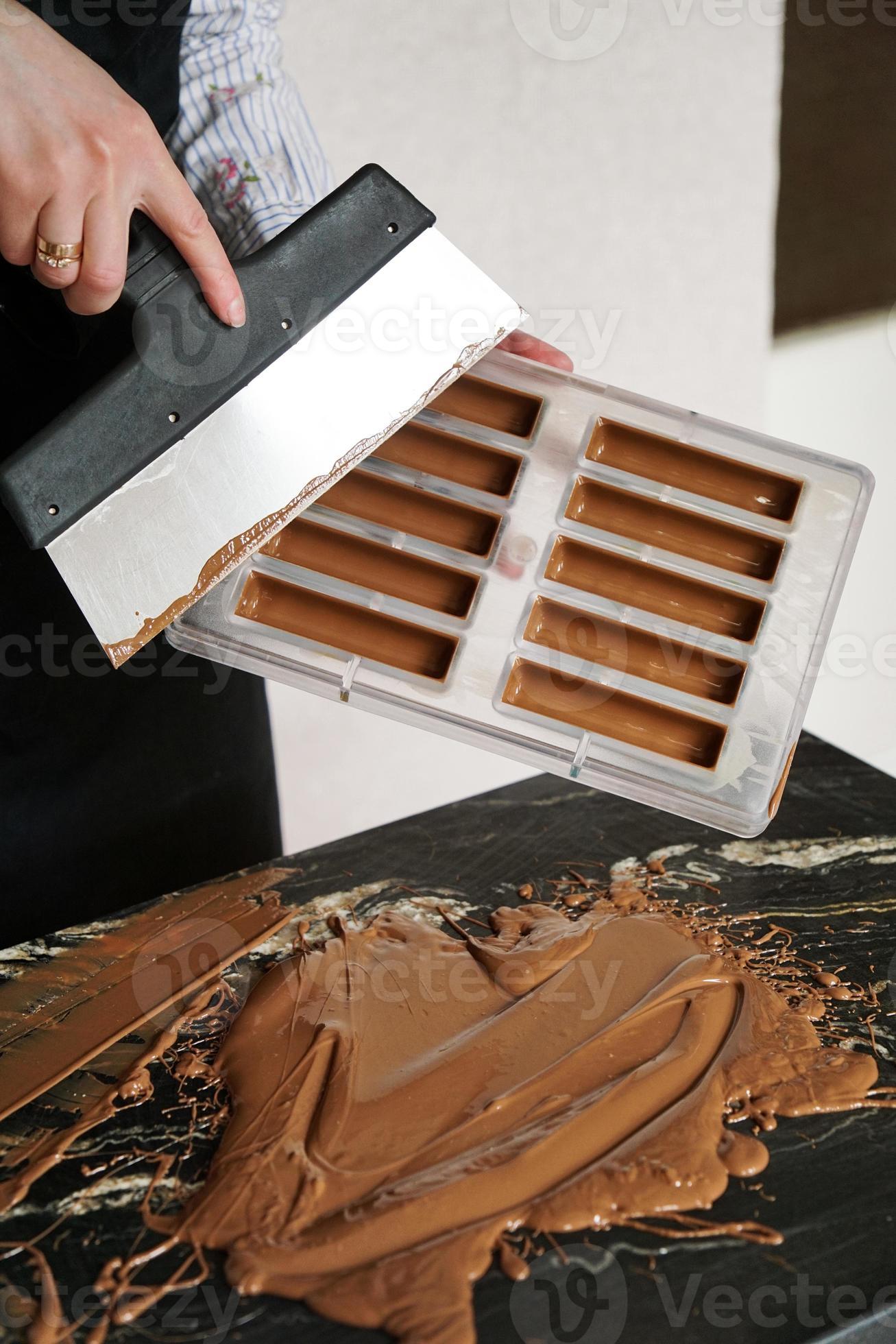 Confectioner removes the remaining chocolate with a spatula from a