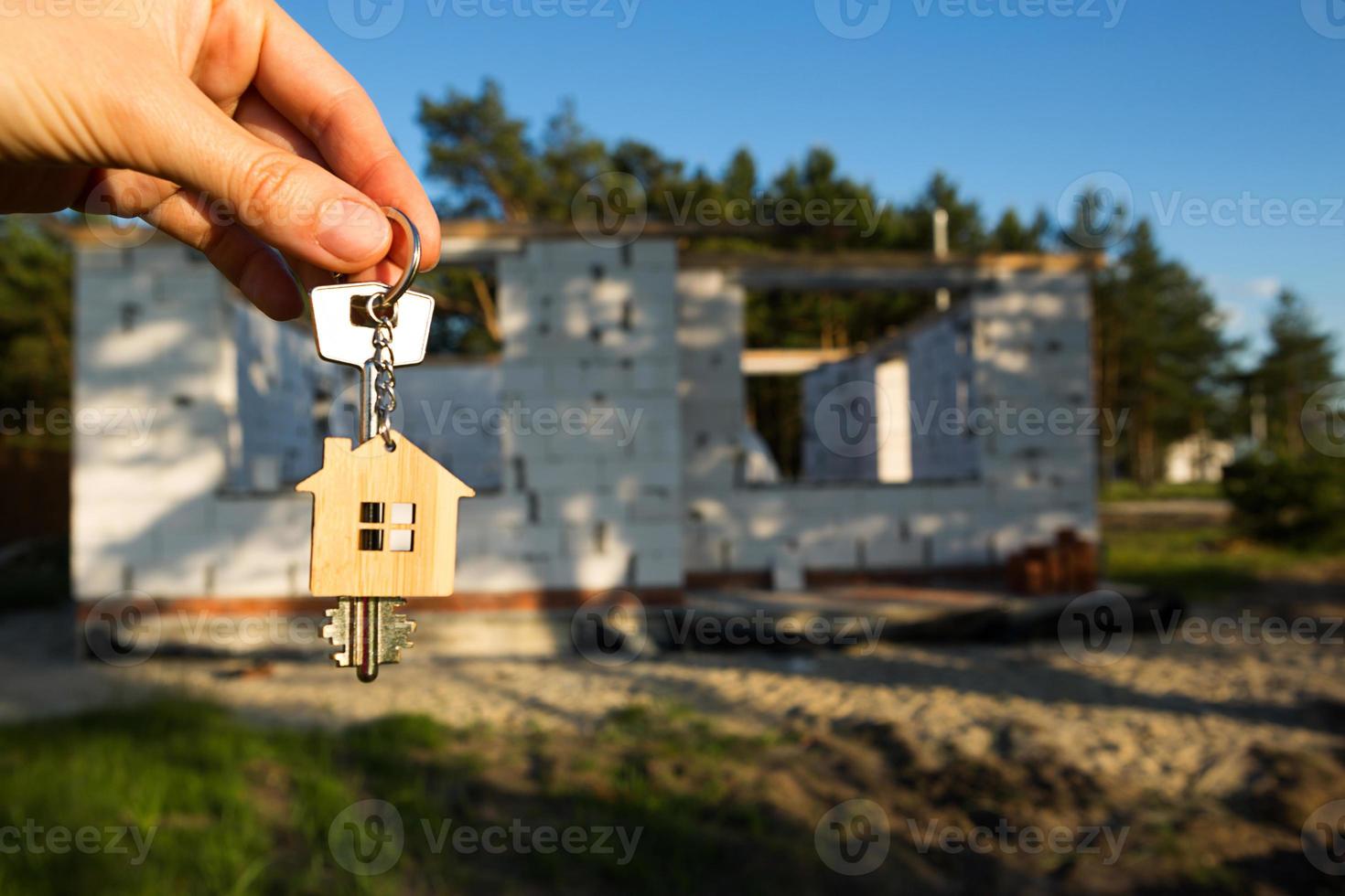 Hand with the key to the future house on the background of a construction site and walls made of porous concrete block. Building a home, moving to a new cottage, farm in the countryside photo
