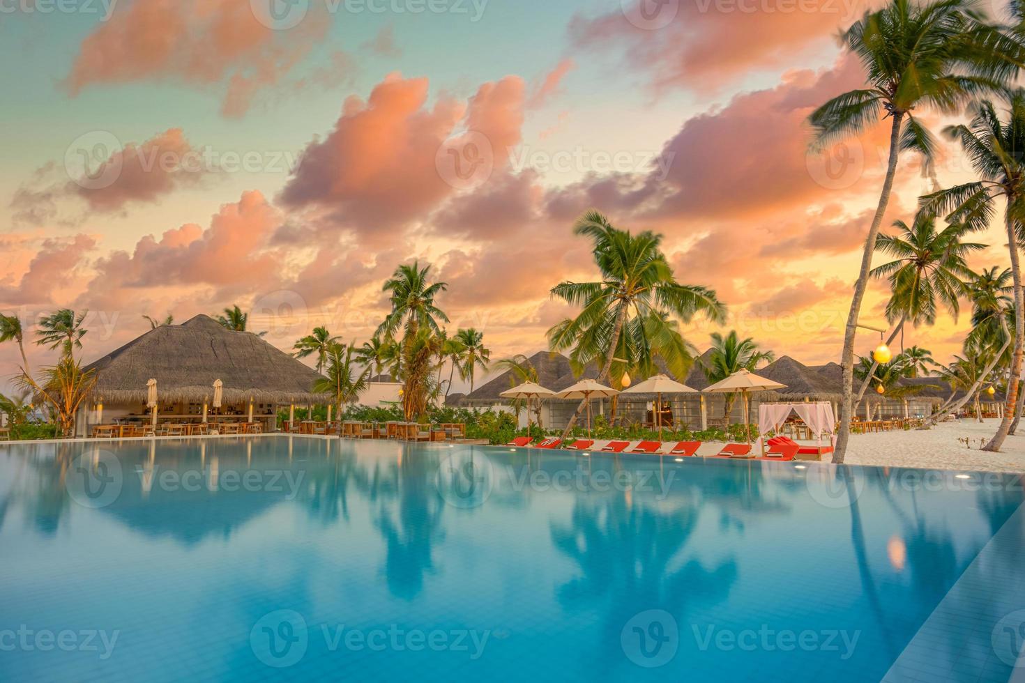 Luxury sunset over infinity pool in a summer beachfront hotel resort at tropical landscape. Tranquil beach holiday vacation background mood. Amazing island sunset beach view, palms swimming pool photo
