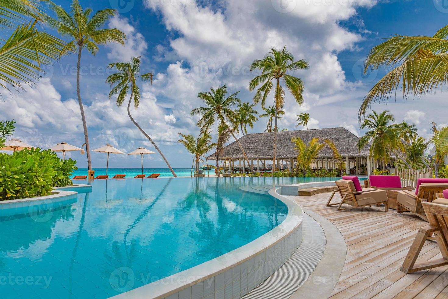 Outdoor tourism landscape. Luxurious beach resort with swimming pool and beach chairs or loungers under umbrellas with palm trees and blue sky. Summer travel and vacation background concept photo