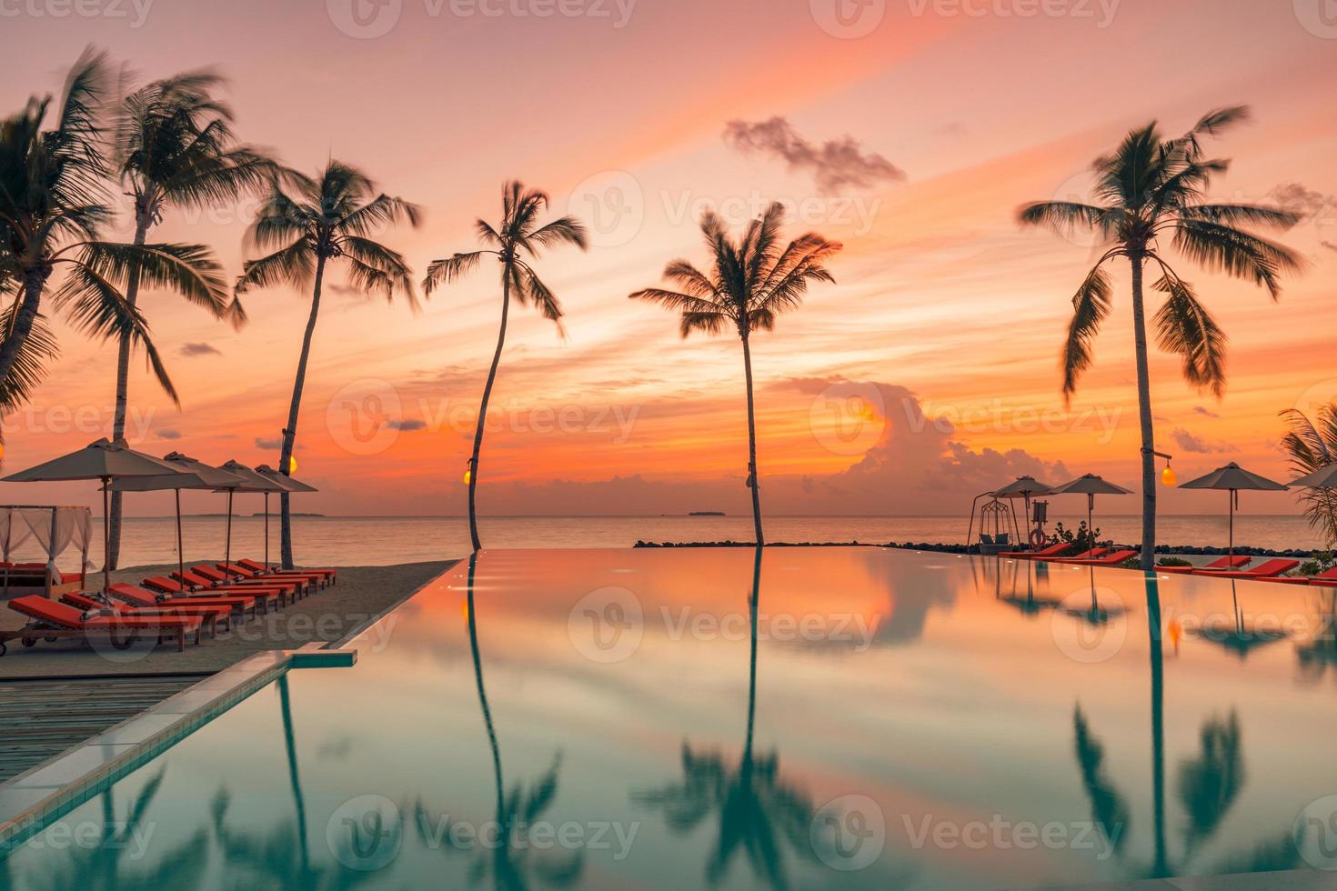 Perfect beach sunset, relaxation pool in a luxurious beachfront hotel resort in sunset light perfect beach holiday vacation banner. Sunset beach landscape. Loungers palm tree infinity pool reflections photo