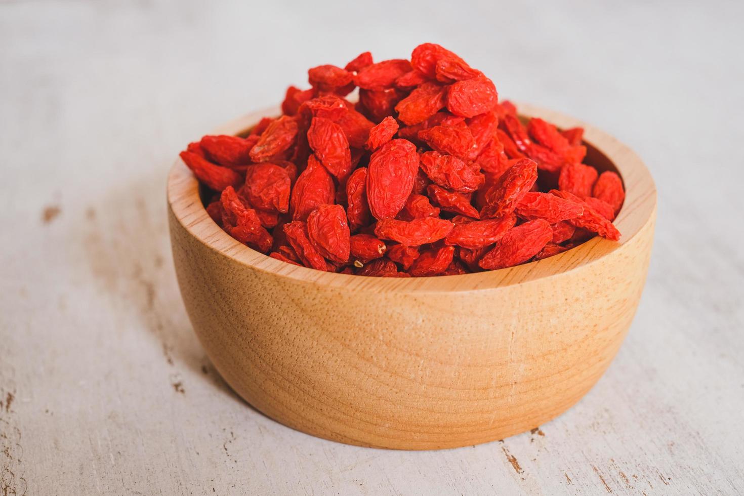 Dried Chinese wolfberries or Goji berry chinese herb or Matrimony vine in the woodden scoop on wooden bowl isolated on wooden background.  Selected focus. photo