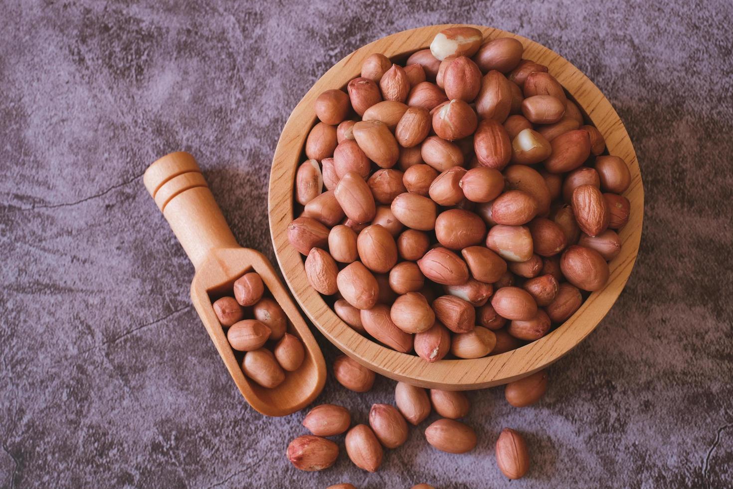Raw Groundnuts in the wooden bowl on cement background. Top view. photo