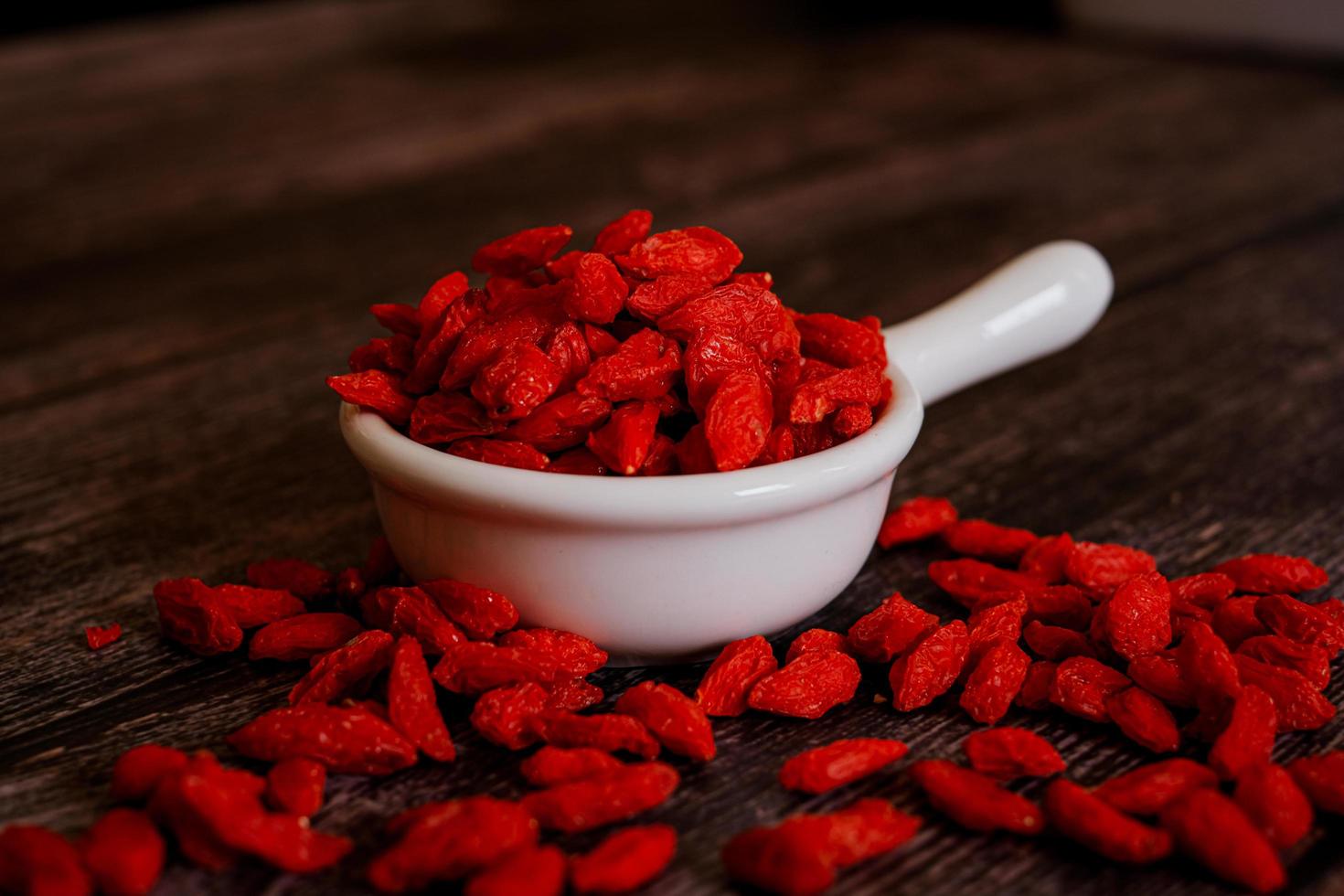 Dried Chinese wolfberries or Goji berry chinese herb or Matrimony vine in the white ceramic bowl isolated on wooden background.  Selected focus. photo