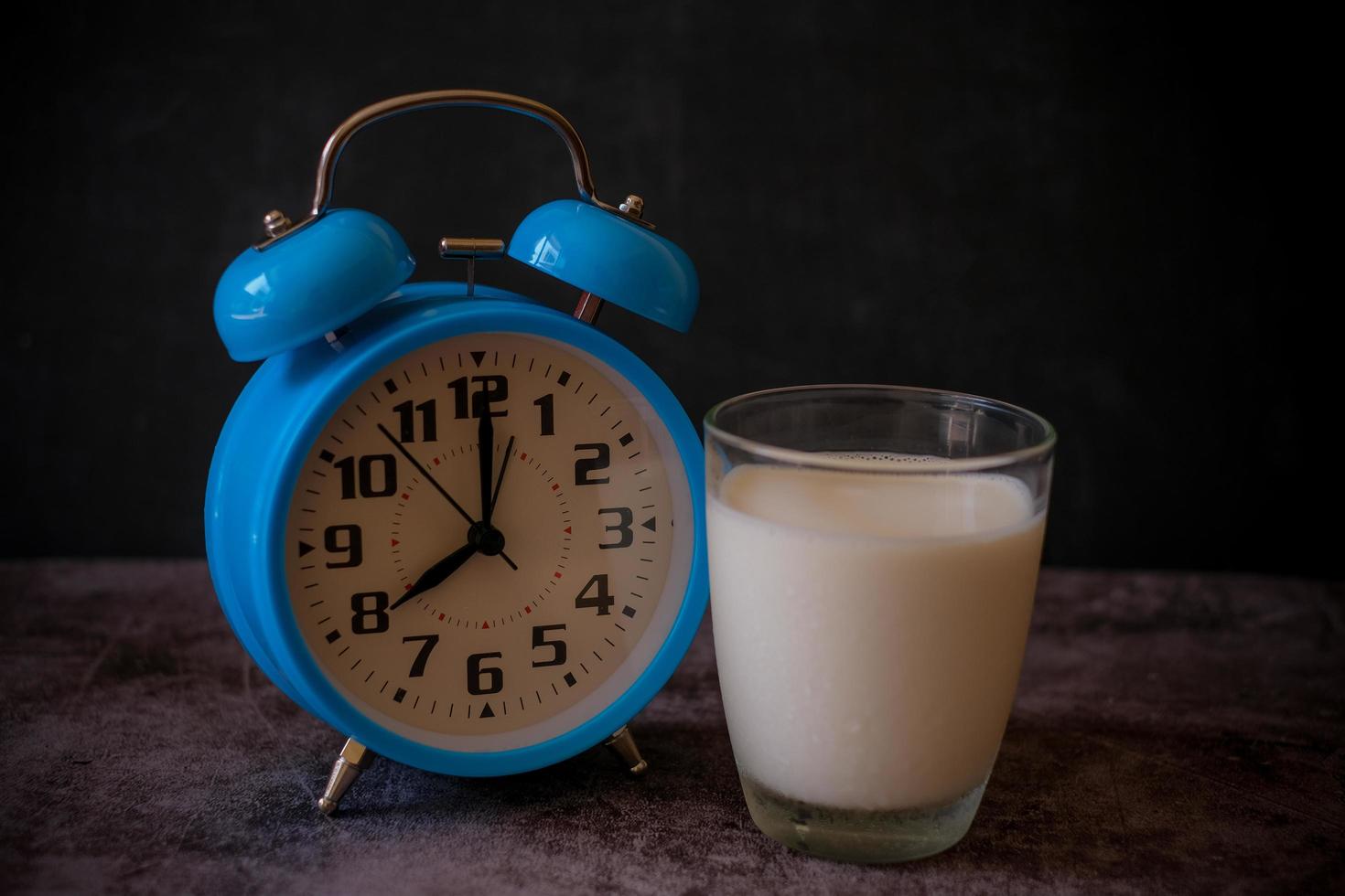 Close up a glass of milk and blue vintage alarm clock. 20.00 o'clock late evening and time to go to bed. Healthy sleep, sweet dreams concept. 8.00 o'clock morning time for breakfast concept. photo