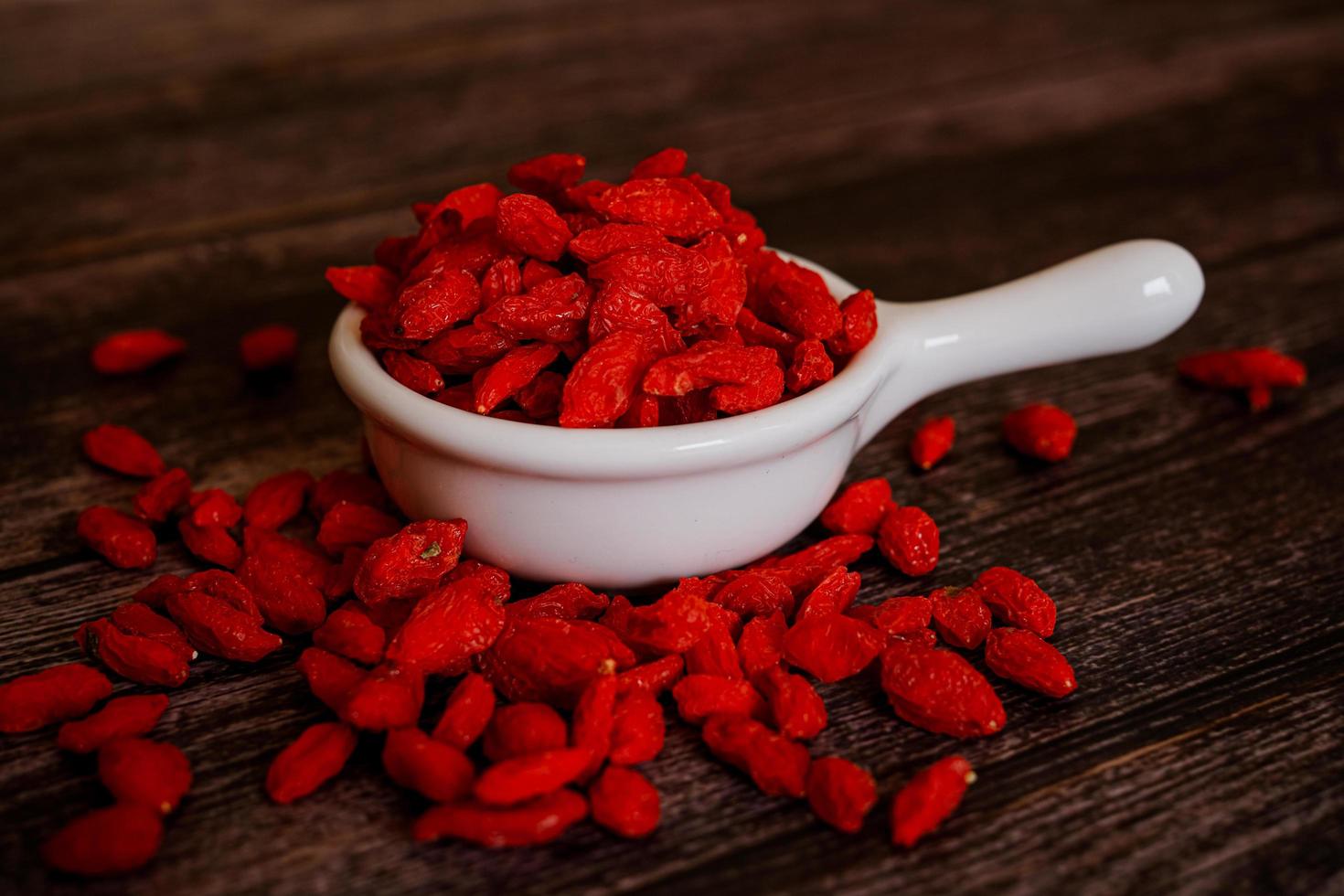 Dried Chinese wolfberries or Goji berry chinese herb or Matrimony vine in the white ceramic bowl isolated on wooden background.  Selected focus. photo