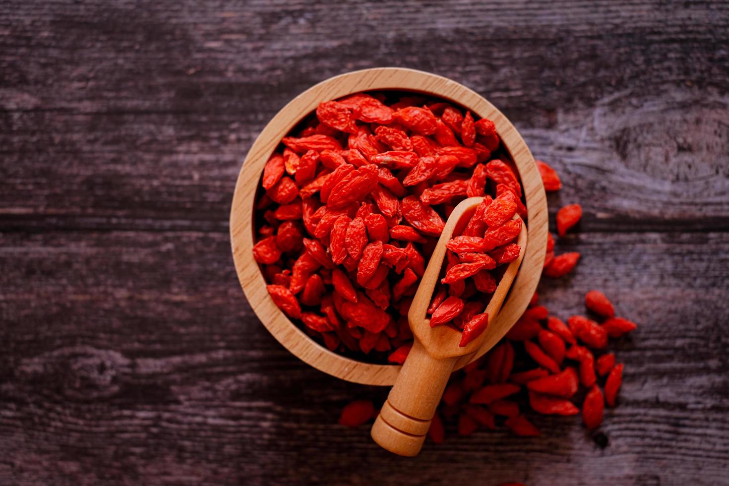 Dried Chinese wolfberries or Goji berry chinese herb or Matrimony vine in the woodden scoop on wooden bowl isolated on wooden background.  Selected focus. photo