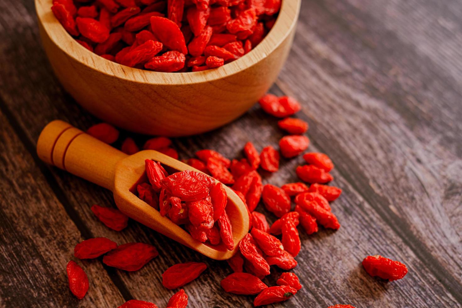 Dried Chinese wolfberries or Goji berry chinese herb or Matrimony vine in the woodden scoop on wooden bowl isolated on wooden background.  Selected focus. photo