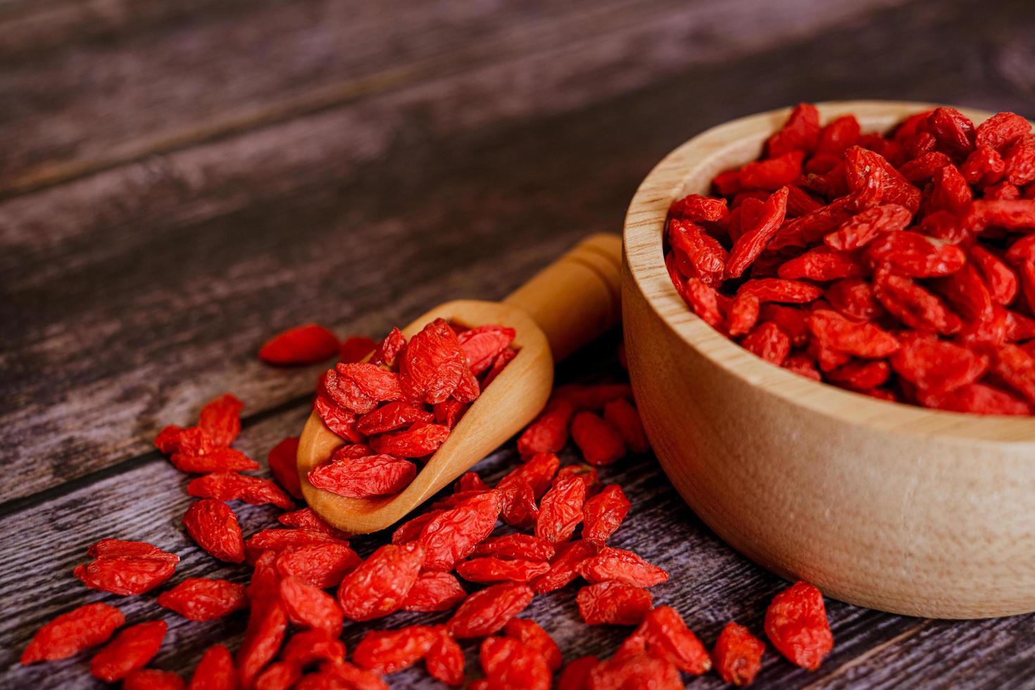Dried Chinese wolfberries or Goji berry chinese herb or Matrimony vine in the woodden scoop on wooden bowl isolated on wooden background.  Selected focus. photo
